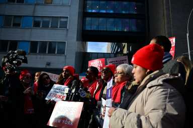 group of people holding signs, some wearing red hats during a nurses strike in NYC