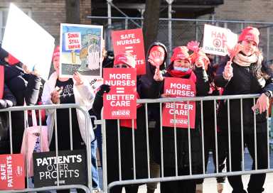 group of people wearing red behind metal barrier during nurses strike