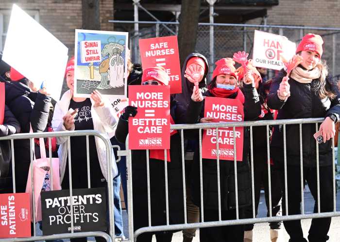 NURSES STRIKE: Contract talks continue between caretakers and hospitals; progress made at NewYork-Presbyterian 2 group of people wearing red behind metal barrier