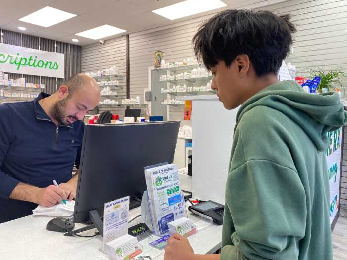 a man behind a counter in a pharmacy assisting a patient