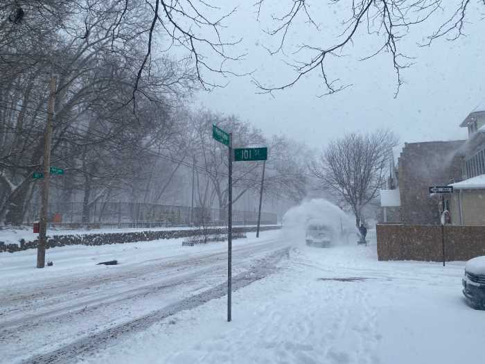a snowy intersection where a man is using a snowblower 