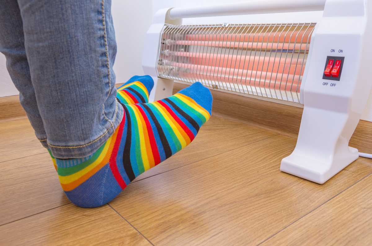 How to stay warm in NYC during a freeze: Tips for tackling heat issues, icy sidewalks and more 2 A person wearing bright rainbow-colored socks and warms cold feet near an electric space heater in winter. Infrared halogen heater at home.