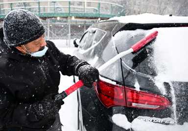 winter storm man clears snow off windshield of car