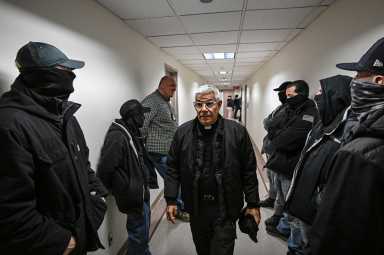 Father Fabian Arias walking past ICE agents while advocating for immigrants
