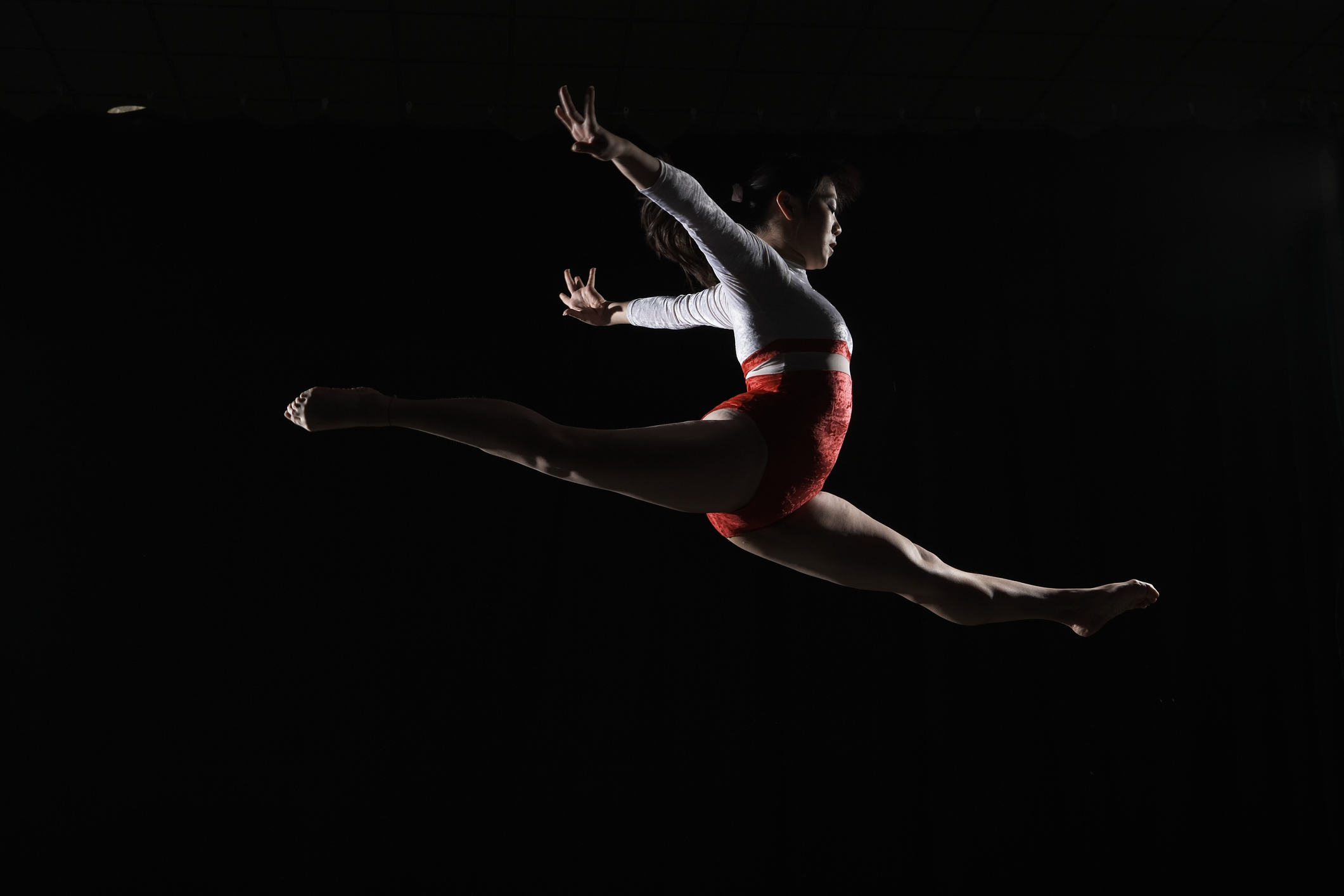 Young female gymnast leaping in midair, arms outstretched, side view