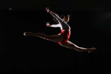 Young female gymnast leaping in midair, arms outstretched, side view